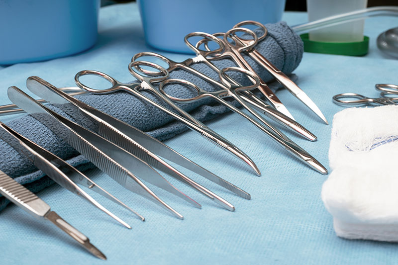 Surgical instruments lined up on table including tweezers, scissors and forceps