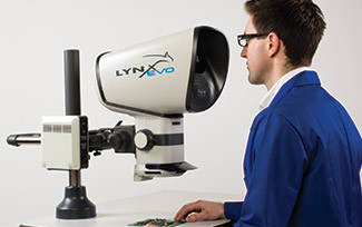 man in in blue overall wearing glasses looking through a Lynx EVO stereo microscope