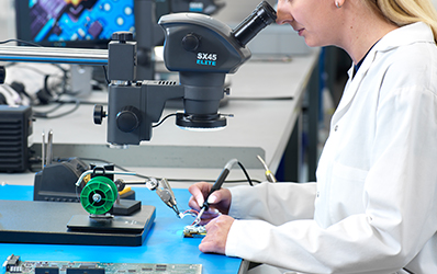 Woman in white coat soldering with SX45 stereo microscope