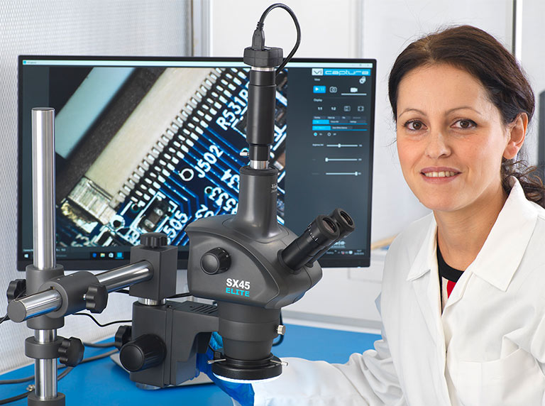 Technician next to a SX Elite trinocular stereo microscope displaying PCB on monitor