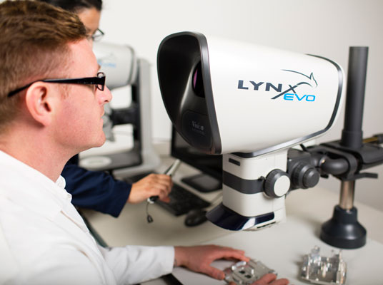 Man wearing glasses operating Lynx EVO stereo zoom microscope in lab