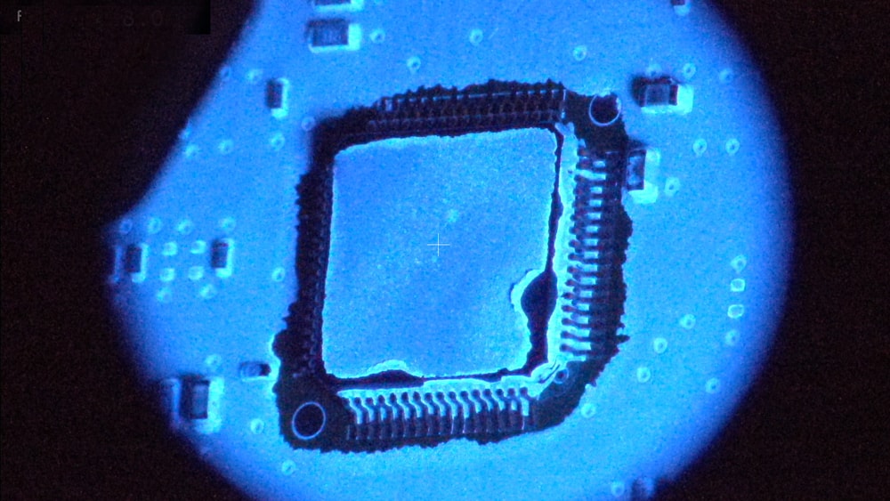 Surface mount component under blue UV illuminated to inspect conformal coating