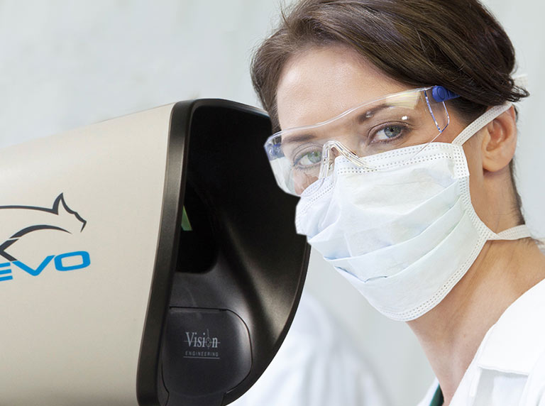 woman wearing protective glasses and mask next to a Lynx EVO stereo zoom microscope