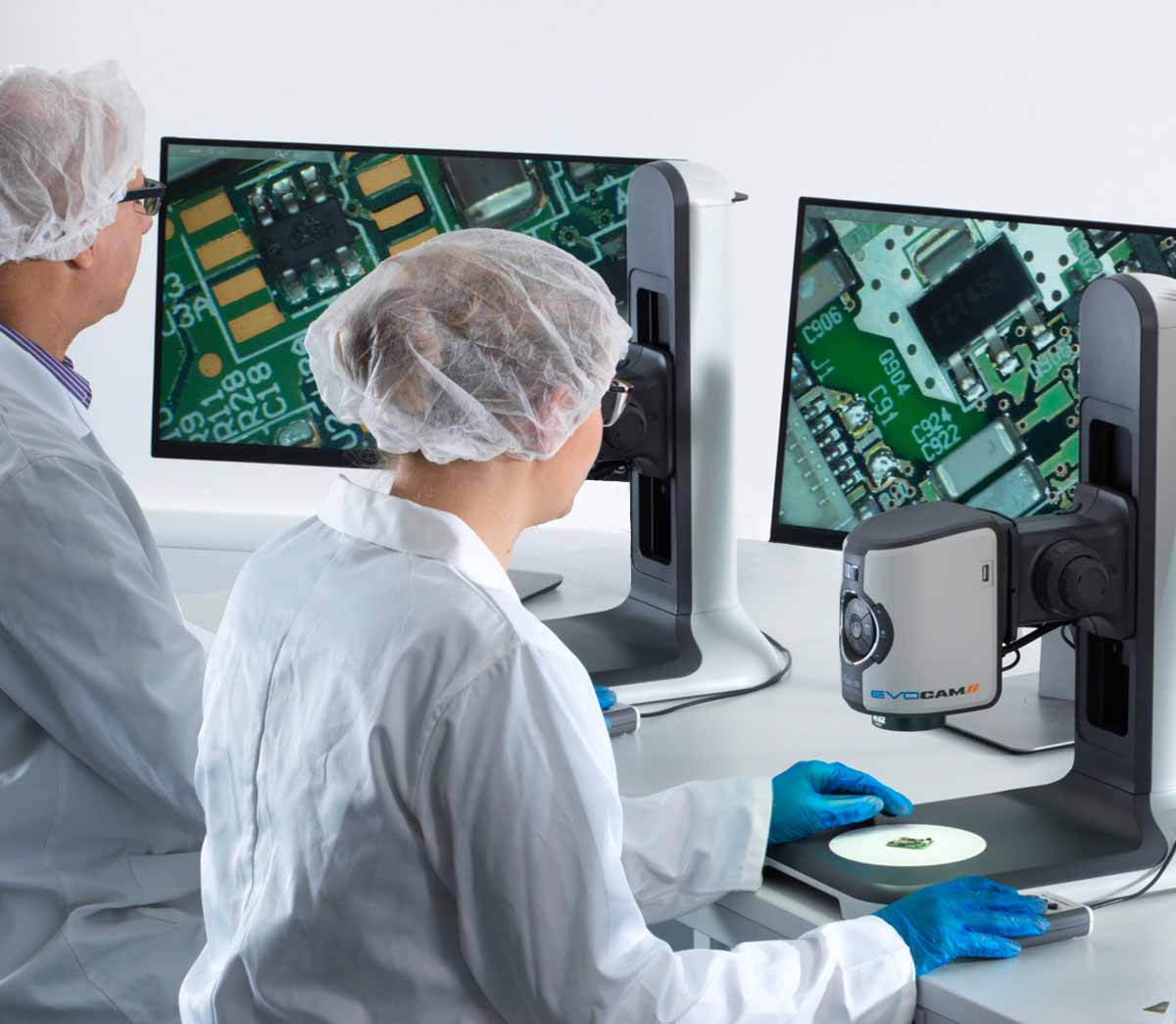 Operator in white coats, hair nets and glasses inspection electronics PCB using EVO Cam II digital microscope