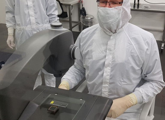 Man in white overall in clean room looking through Falcon Video measuring system