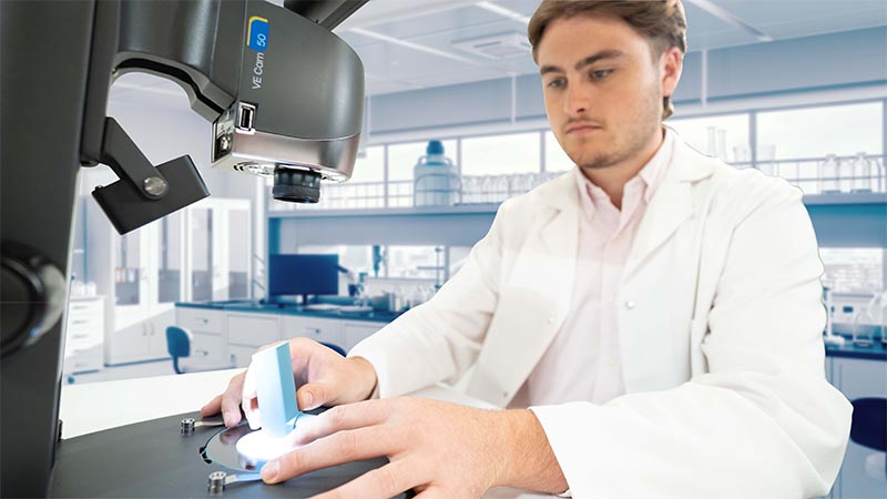 man in white coat looking at part under VE Cam digital microscope