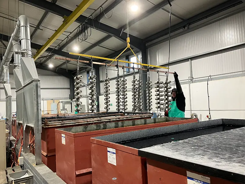 Man operating large crane over large anodising tanks, he is about to submerge multiple components 